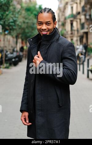 Confident and stylish African American man looking at camera and smiling while posing outdoors on the street. Stock Photo