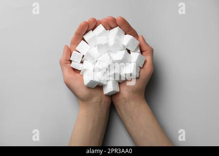 Woman with handful of styrofoam cubes on light grey background, top view Stock Photo