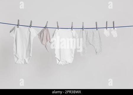 Different baby clothes drying on laundry line against light background Stock Photo