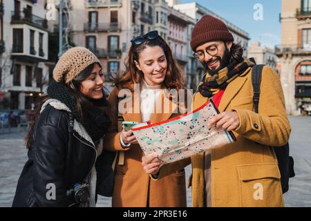 Group of tourists reading a map to found the location of a european monument. Three young travelers watching a guide looking directions visiting Barcelona city in a journey trip. Friends sightseeing. High quality photo Stock Photo