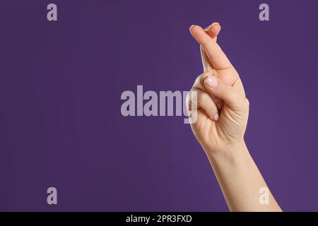 Woman holding fingers crossed on purple background, closeup with space for text. Good luck superstition Stock Photo