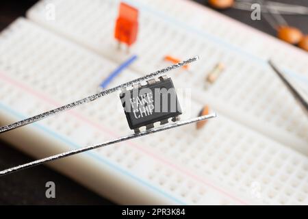 Fake chip concept: An integrated circuit held with tweezers on top of a breadboard populated with electronic components Stock Photo