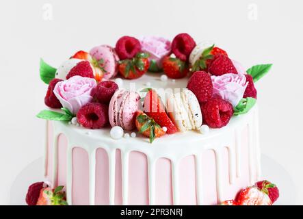 Birthday sweet cake with berries, macaron and floral decor on table. Beautiful pink cake decorated with macarons, raspberries, strawberries and sugar Stock Photo