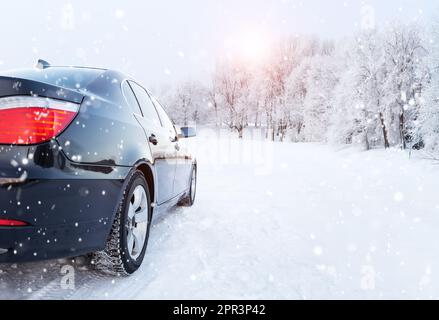 Black car on a winter road in a snowy forest, winter journey. Modern car with winter tires on snowy road Stock Photo