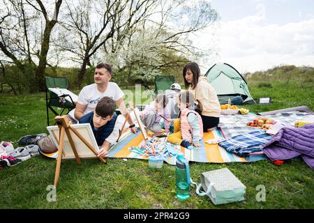 https://l450v.alamy.com/450v/2pr42g9/happy-young-family-with-four-children-having-fun-and-enjoying-outdoor-on-picnic-blanket-painting-at-garden-spring-park-relaxation-2pr42g9.jpg