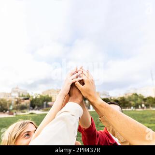 Diverse young adult people stacking hands showing unity outdoors. Stock Photo
