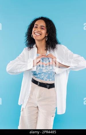 carefree african american woman in white stylish shirt showing heart sign with hands isolated on blue,stock image Stock Photo