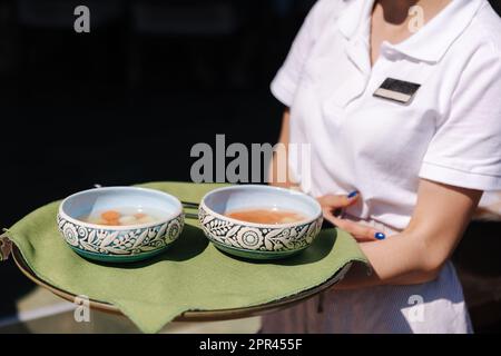 Middle selection of waitress hold two portion of soup on a tray. Fresh vegan soup in restaurant. Service  Stock Photo