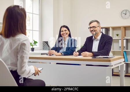 Young woman is being interviewed by two friendly, smiling business partners, colleagues are listening to potential new employee. Stock Photo