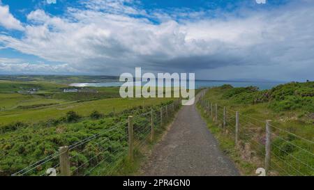 Walking and hiking trails in green hills of Giant's Causeway, Ireland, with an ocean view, blue sky with clouds and an Irish village in the background Stock Photo