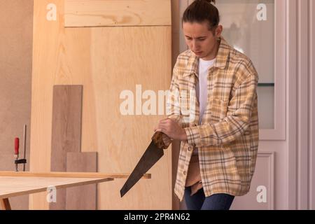 Young concentrated woodworker in workwear sawing lumber plank while working in professional joinery workshop Stock Photo