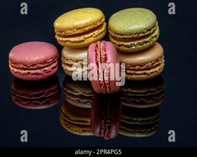 A group of delicious and colorful macarons are reflected on the glossy black support base Stock Photo
