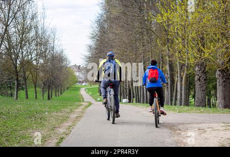 Senior man and woman are exercising on bicycles outdoors, they are a couple. Back view . Stock Photo