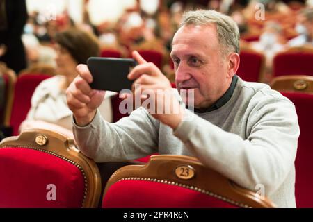 caucasian senior takes pictures on a smartphone in the theater hall Stock Photo