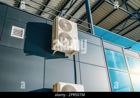 Industrial air conditioner installed on exterior metal wall of modern office building. Sun reflected in window. Stock Photo