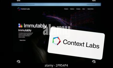Person holding mobile phone with logo of Dutch blockchain company Context Labs B.V. (CXL) on screen in front of web page. Focus on phone display. Stock Photo