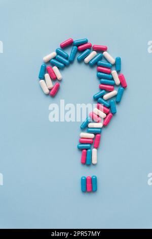 Question mark consisting of three multi-colored vitamins on a blue background. Health problems and treatment. The concept of evidence-based medicine Stock Photo