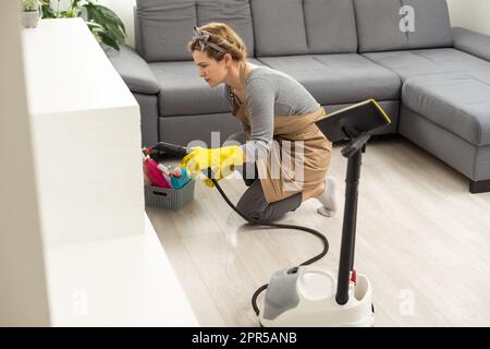 The woman washes the floor in the room with a white steam cleaner, a wet high-pressure steam. Cleaning of the apartment. we kill microbes Stock Photo