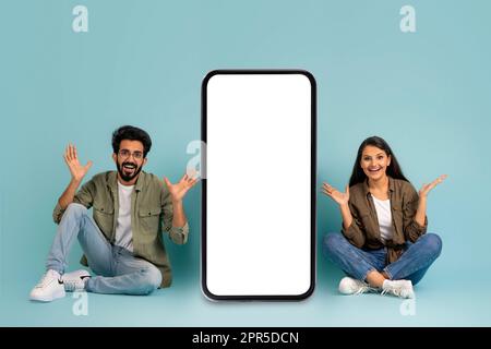 Positive eastrn couple sitting by big cell phone, mockup Stock Photo