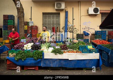 Vegetable vendor sells eggplants carrots and turnips from his stall at a European farmer's market in Athens Stock Photo