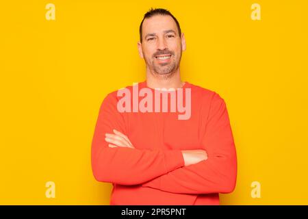 Portrait of a smart, cheerful and attractive bearded Hispanic man in his 40s, arms crossed, isolated over yellow colored background. Stock Photo