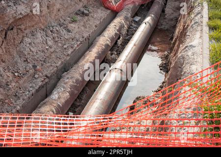 Repair of the heating plant system with the laying of new underground metal pipes in the trench. Reconstruction of the city heating system. Mesh fencing for work safety Stock Photo