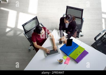 Two asian businesswoman meeting in modern office with laptop computer, tablet, document folder and coffee on table. People corporate business team concept. Top View Stock Photo
