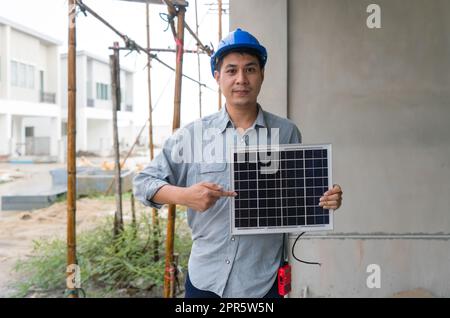 Young engineer in hardhat and walkie talkie pointing finger at solar cell panel, present a source of energy to generate direct current electricity. Stock Photo