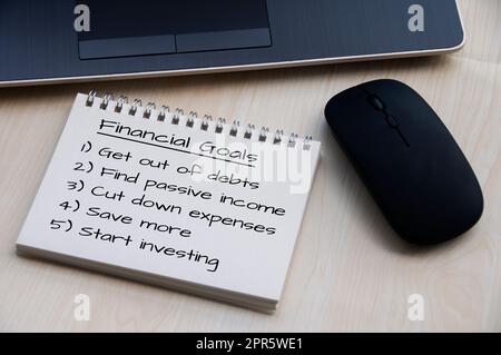 Financial goals on notepad on blank notepad with laptop and mouse on a wooden table. Stock Photo