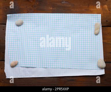 white sheet of paper in a cage on a brown wooden background, place for an inscription Stock Photo