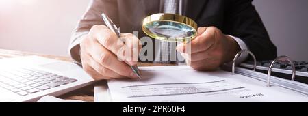 Businessperson Looking At Receipts Through Magnifying Glass Stock Photo