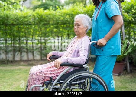 Doctor caregiver help and care Asian senior or elderly old lady woman patient sitting on wheelchair in park at nursing hospital, healthy strong medical concept Stock Photo