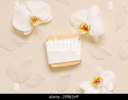 Handmade soap bar near white orchid flowers on light yellow top view. Mockup Stock Photo