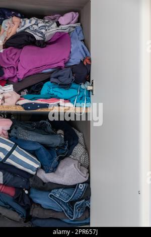 Chaotic wardrobe and sloppy closet shows many outfits of a woman with shopping addiction and many clothes like pullovers, shirts and trousers as crumpled laundry stored into a messy heap of fashion Stock Photo