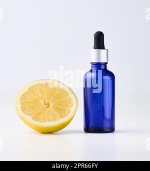 Blue glass bottle with pipette, next to it is half a lemon on a white front. Stock Photo