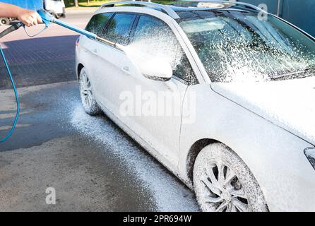 Hand washing with high pressure water in a car wash outside. A jet of foam. The concept of hand washing, self-service. Stock Photo