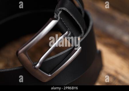Black men's belt for pants on an aged vintage wooden background. Close up of metal belt buckle Stock Photo
