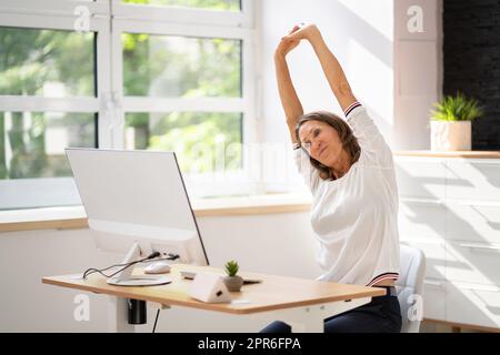 Woman Stretches At Office Desk Stock Photo