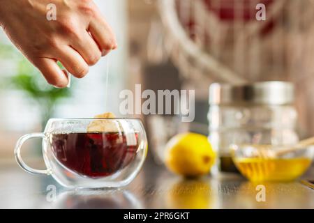 Woman puts the tea bag in the glass cup with hot water Stock Photo