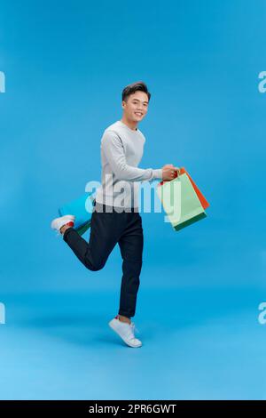 Full size photo of crazy handsome guy hurry rush hold packages jump isolated on blue color background Stock Photo