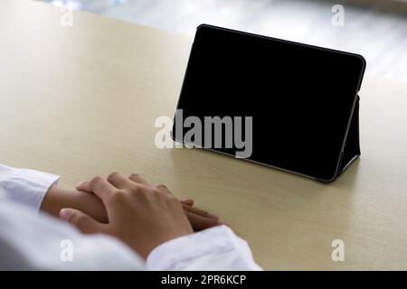 Back view of woman in white gown using a blank screen tablet while sitting at the wooden table. Stock Photo