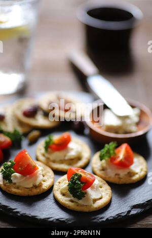 A Glass filled with whiskey soda and Appetizers (crackers, dried fruit, tomatoes, parsley, and cream cheese) Stock Photo