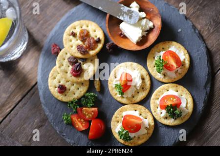 A Glass filled with whiskey soda and Appetizers (crackers, dried fruit, tomatoes, parsley, and cream cheese) Stock Photo