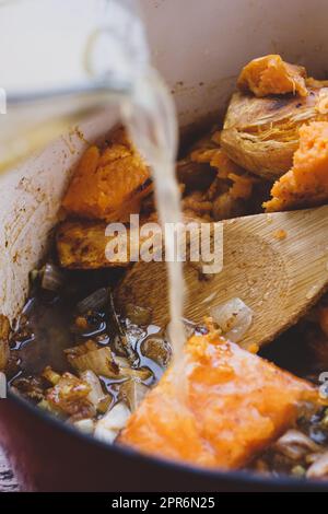 Broth being poured into a pot of sweet potato soup ingredients before it is blended. Recipe process shot. Stock Photo