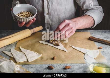 Croissant preparing. Baker sprinkles chopped almonds on top of hazelnut spread Stock Photo