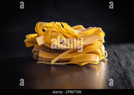 Uncooked pappardelle pasta on black table. Stock Photo