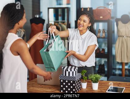 Thank you for your support. Cropped shot of a young store owner handing a parcel to a customer over the counter. Stock Photo