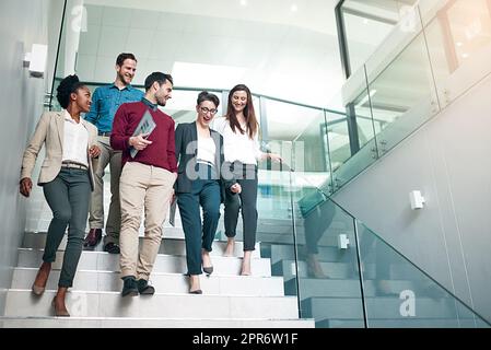 The end of another successful business day. Shot of a group of colleagues talking together while walking down stairs in a large modern office. Stock Photo