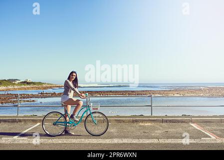 My bike, the sea and me. Portrait of an attractive young woman riding her bicycle outside. Stock Photo