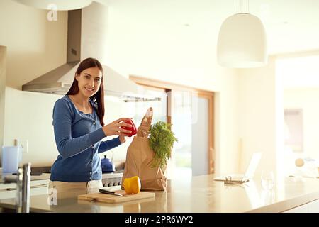 Fresh from the market. Portrait of a happy young woman unpacking a bag of groceries in her kitchen at home. Stock Photo
